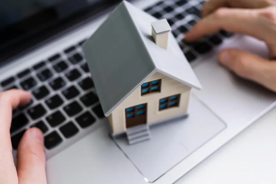 Imagem para hero banner crédito habitação com pc e uma casa por cima do teclado do computador com mãos a mexer no teclado 