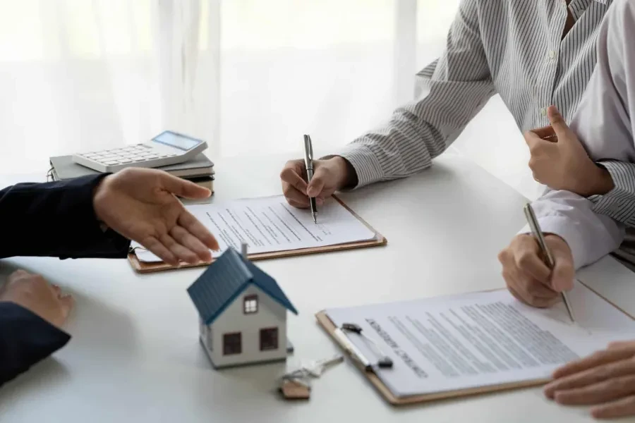 Assinatura de contrato de crédito habitação entre cliente e consultor financeiro, com uma miniatura de casa e chaves sobre a mesa