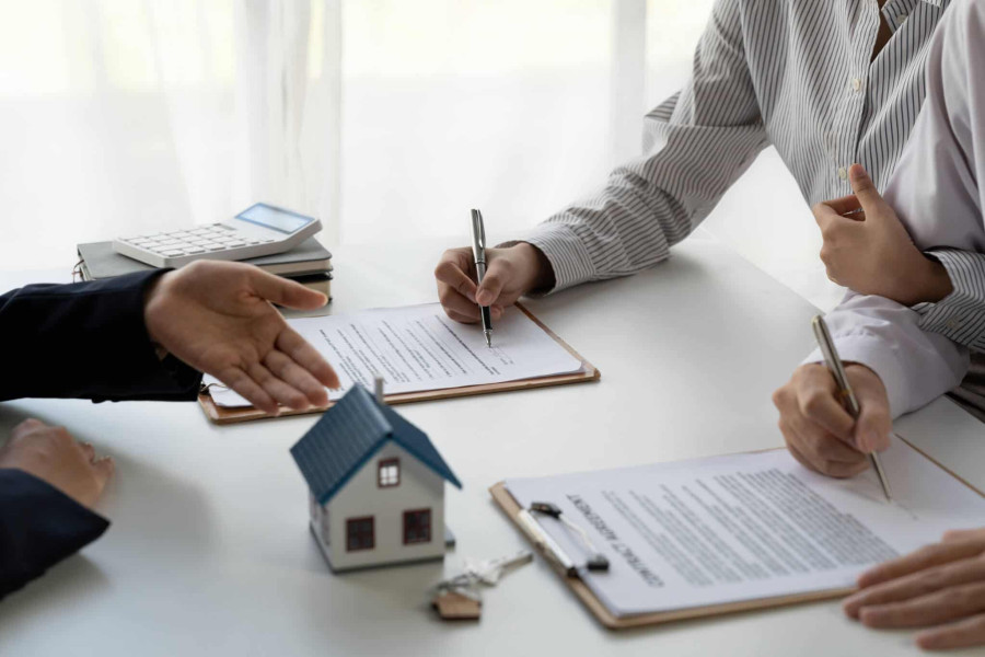Assinatura de contrato de crédito habitação entre cliente e consultor financeiro, com uma miniatura de casa e chaves sobre a mesa