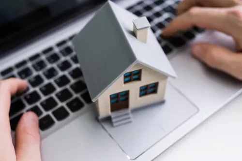 Miniatura de uma casa sobre um portátil, representando a transferência de crédito habitação e poupança nas prestações mensais